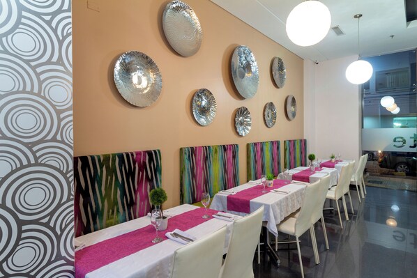 A restaurant with tables set for dining, a colorful abstract wall art, and a modern ceiling design. - Hotel Baroca (Montería)