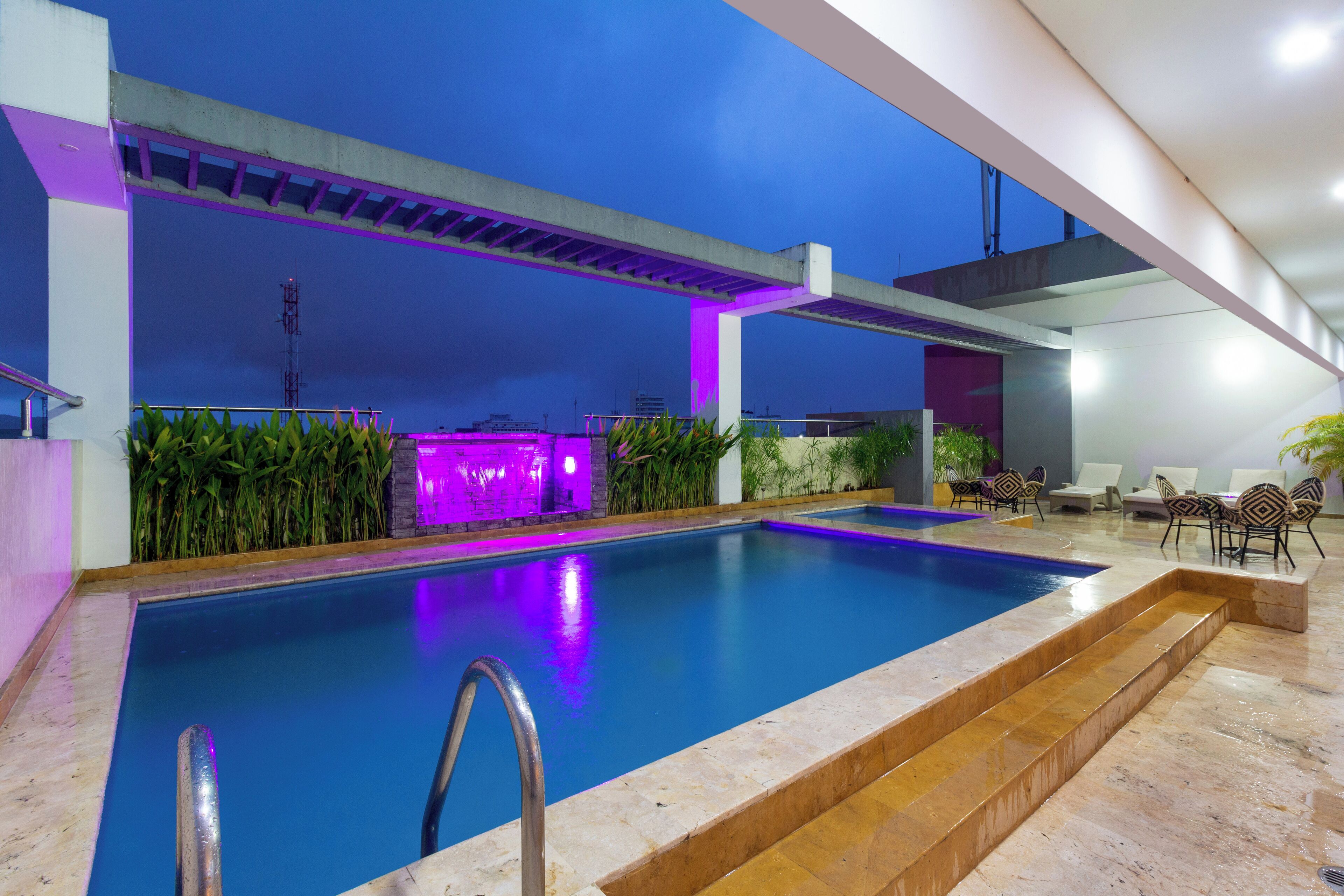 A swimming pool with steps leading into it, surrounded by lounge chairs and a stone wall.