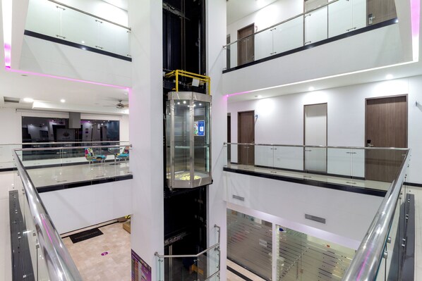 A multi-level interior with glass railings, a central elevator, and a mezzanine with a view of the lower level. - Hotel Baroca (Montería)