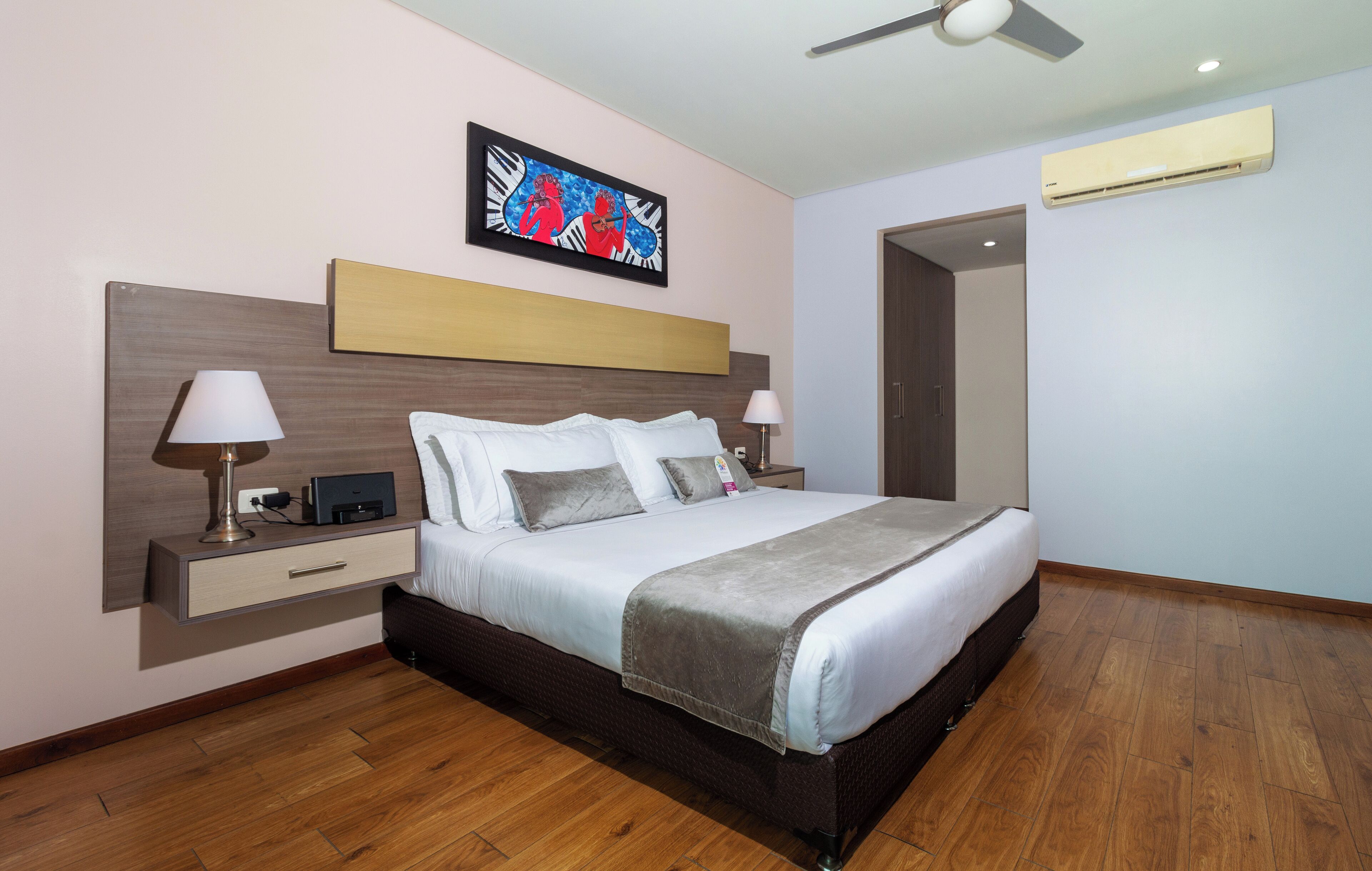 Une chambre d’hôtel moderne dotée d’un grand lit, de lampes de chevet, d’un ventilateur de plafond et d’un climatiseur fixé au mur.