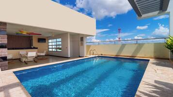 A modern indoor swimming pool with clear blue water, a sunroof, and a view of a tower in the background.