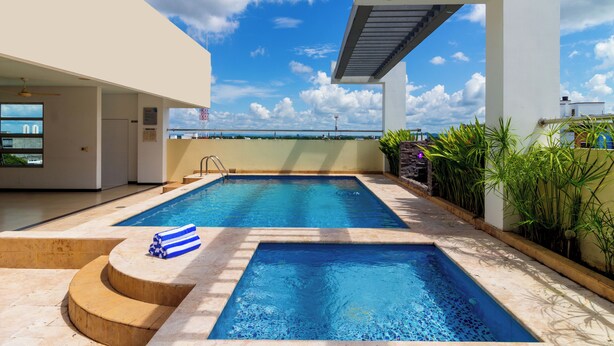 Une piscine sur le toit, avec une eau d’un bleu limpide, entourée d’un bâtiment moderne doté de grandes fenêtres et offrant une vue sur la mer.