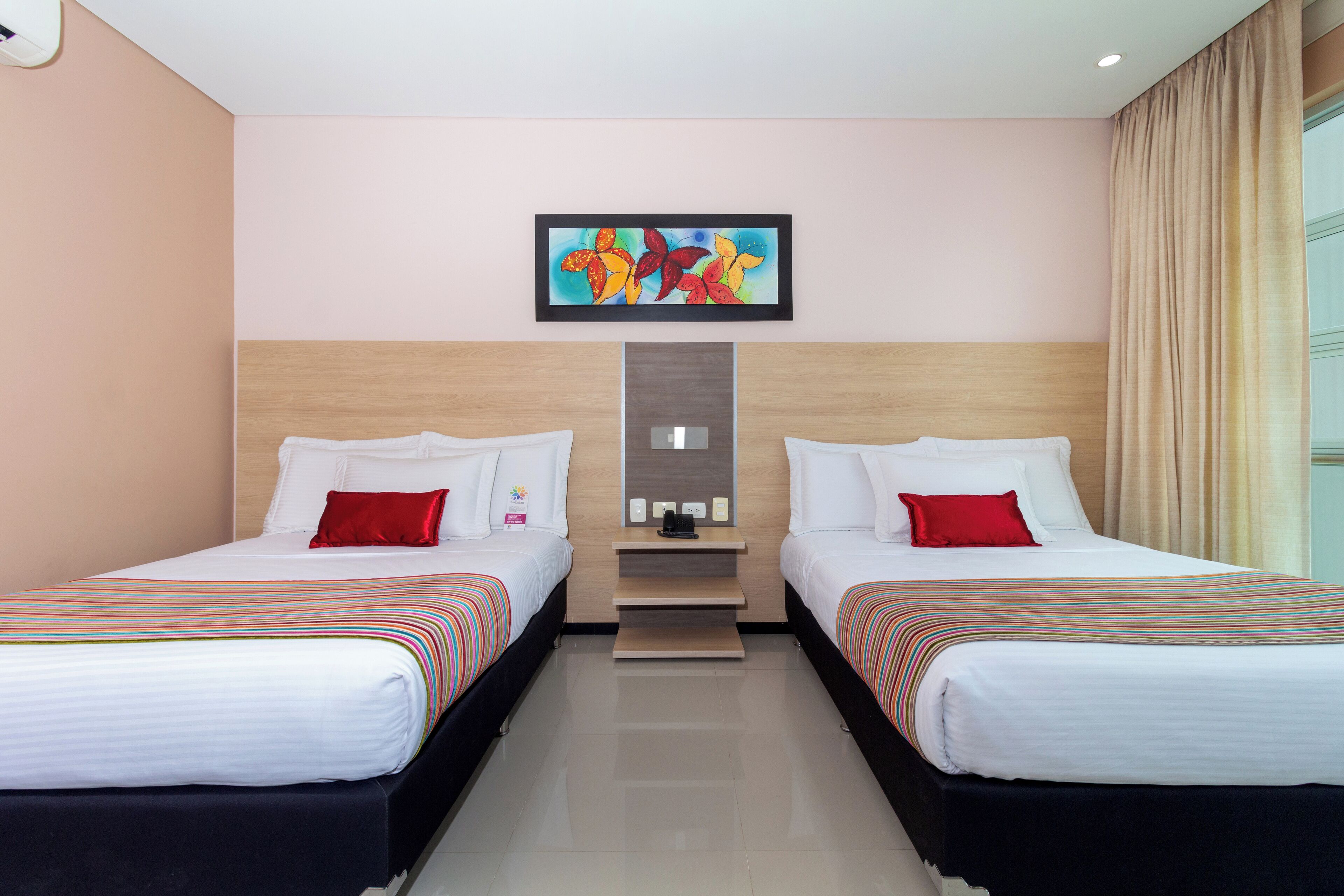Habitación de hotel con dos camas, una mesita y un cuadro en la pared.