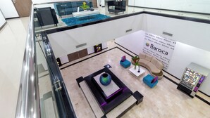 Un hall d’entrée moderne avec une rambarde en verre, un espace détente avec un canapé et des fauteuils, un vase décoratif et un distributeur automatique.
