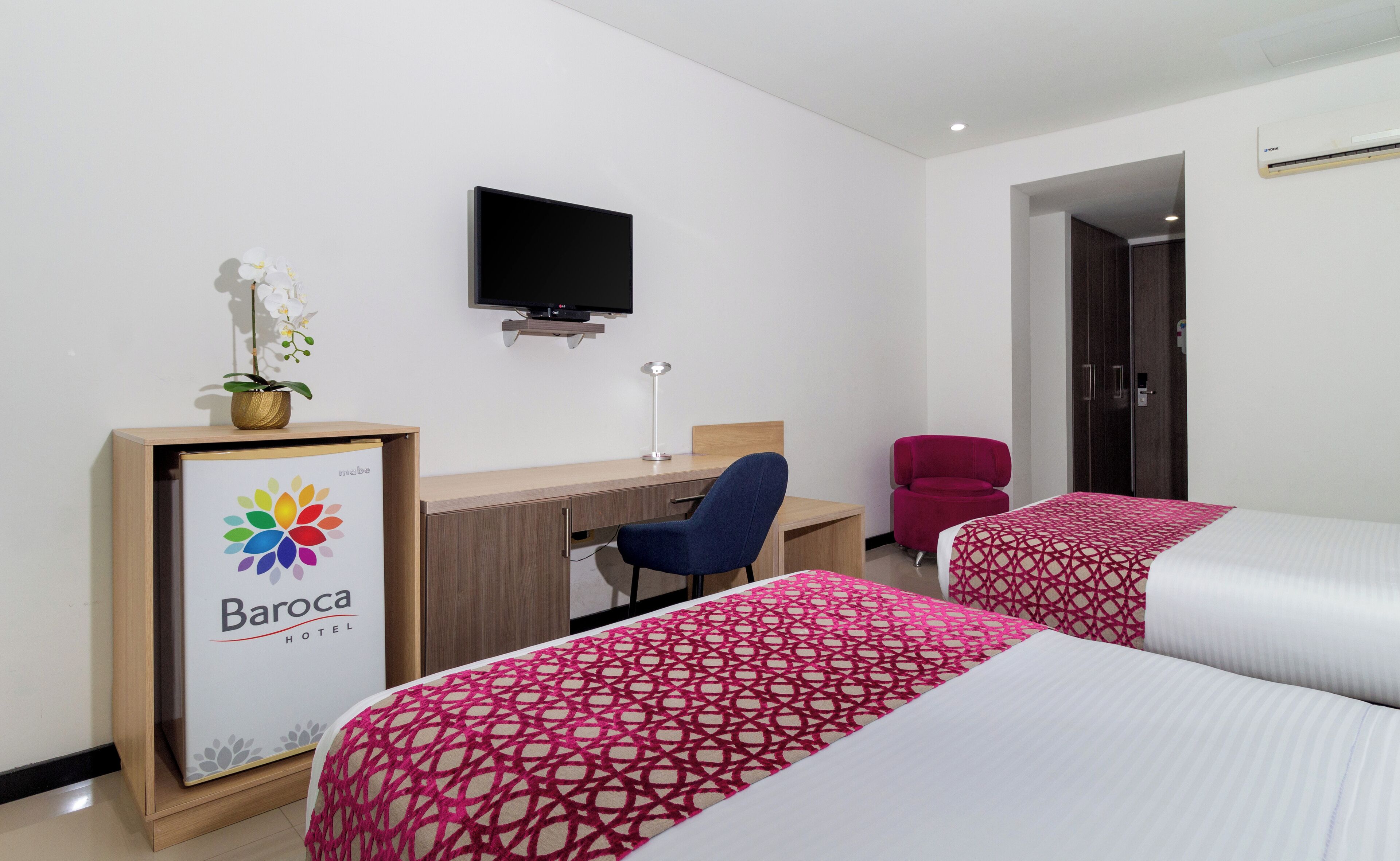 Ein Hotelzimmer mit zwei Betten, einem Schreibtisch, einem Stuhl, einem Fernseher und einem gerahmten Schild.