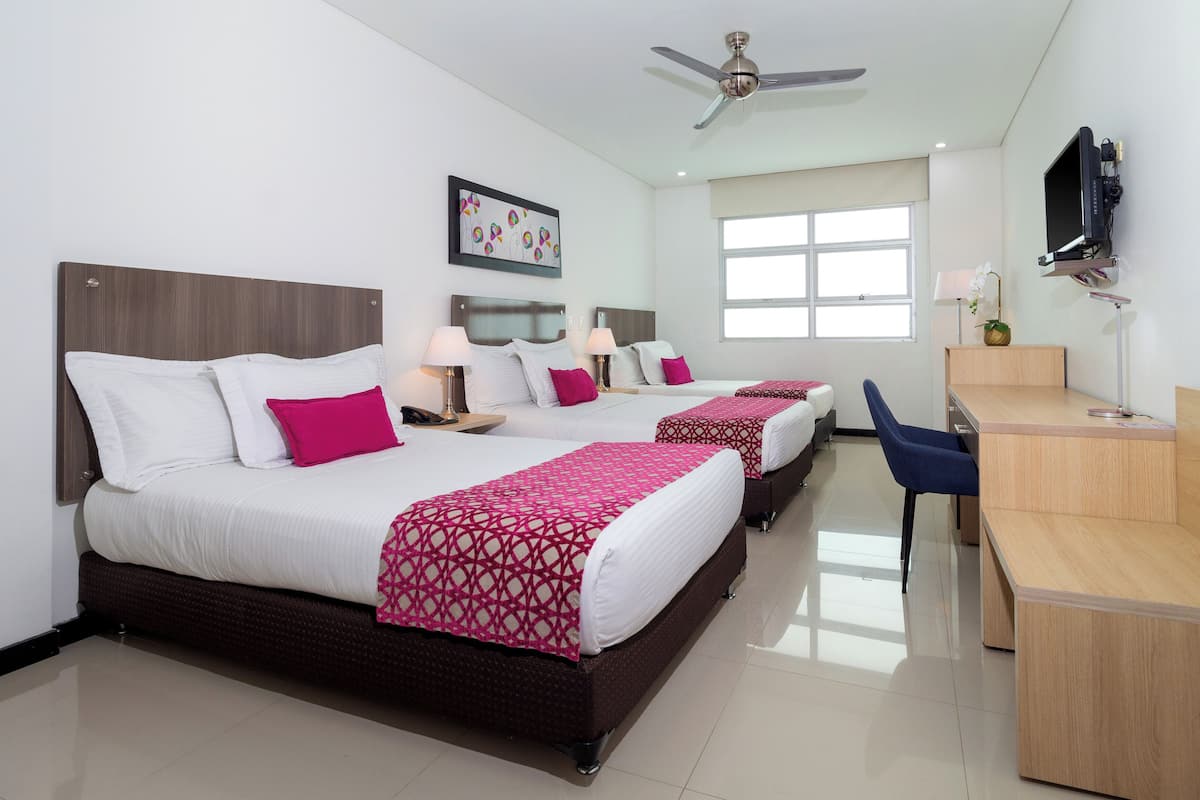 A hotel room with two beds, a desk, a chair, a TV, and a ceiling fan.