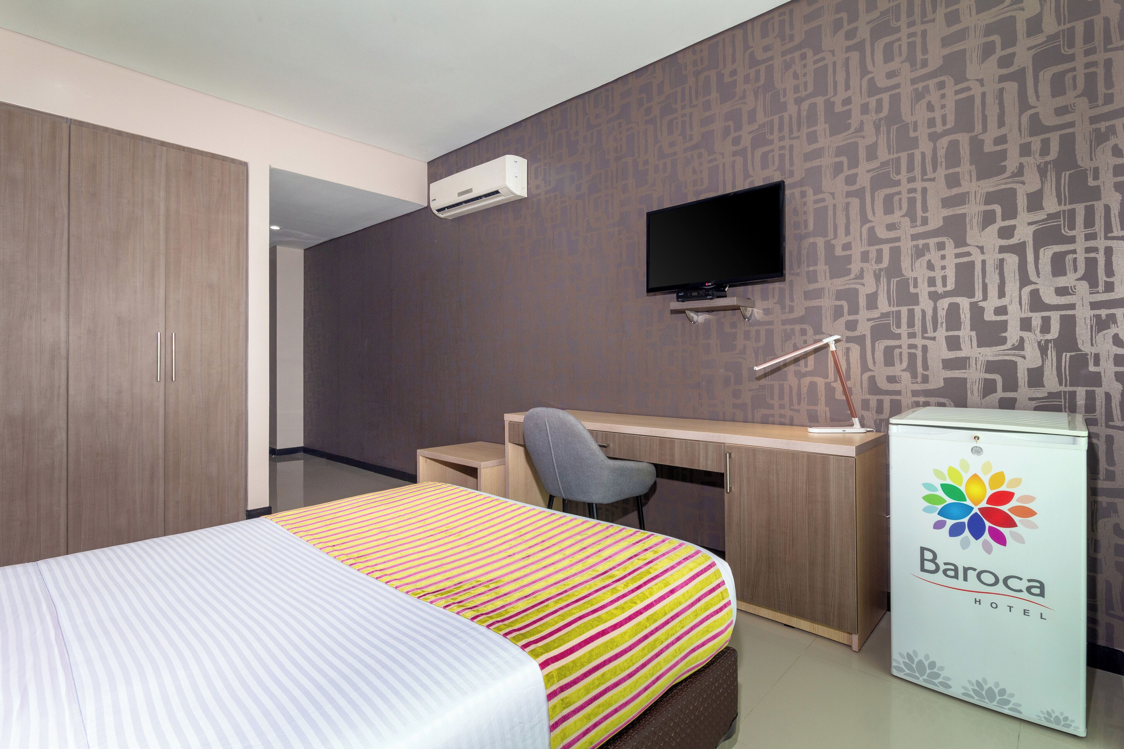 Ein Hotelzimmer mit Bett, Schreibtisch, Stuhl, Fernseher und einer Minibar.