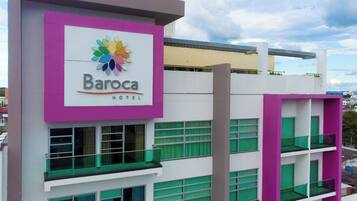 Experience the iconic Baroca Hotel, featuring a striking facade with a leaf-like logo and balconies with views of the surrounding area.