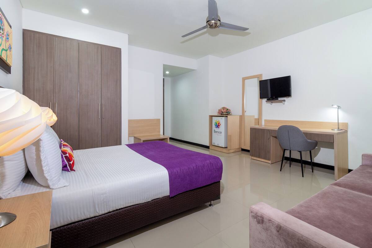 A hotel room with a bed, desk, chair, TV, and a ceiling fan.