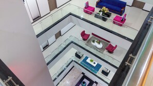 Un atrium à plusieurs niveaux, doté de rampes en verre, d’un canapé bleu, de fauteuils roses et d’une table basse agrémentée de plantes.