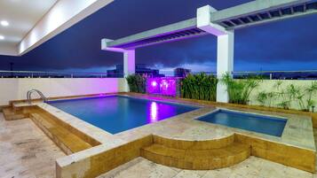 Una piscina en la azotea con jacuzzi, rodeada de plantas y una zona de bar.