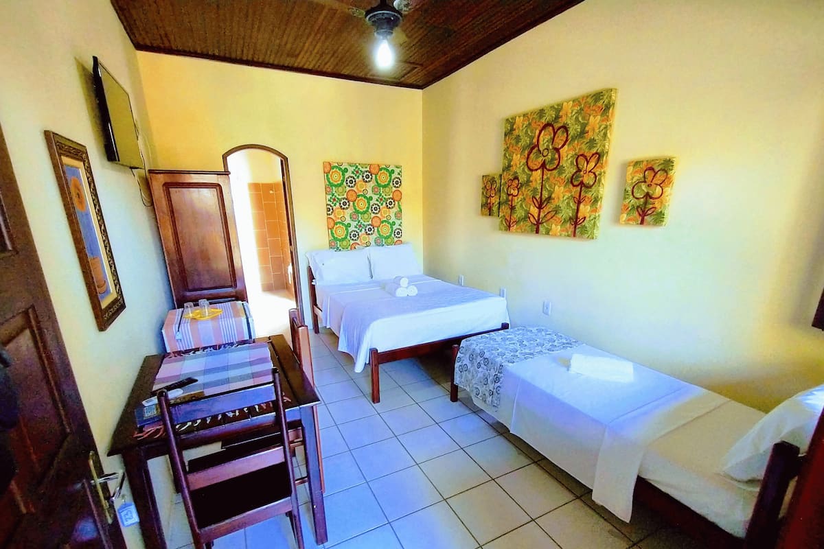 A hotel room with two single beds, a wooden desk with a chair, a mirror, and floral wall art.