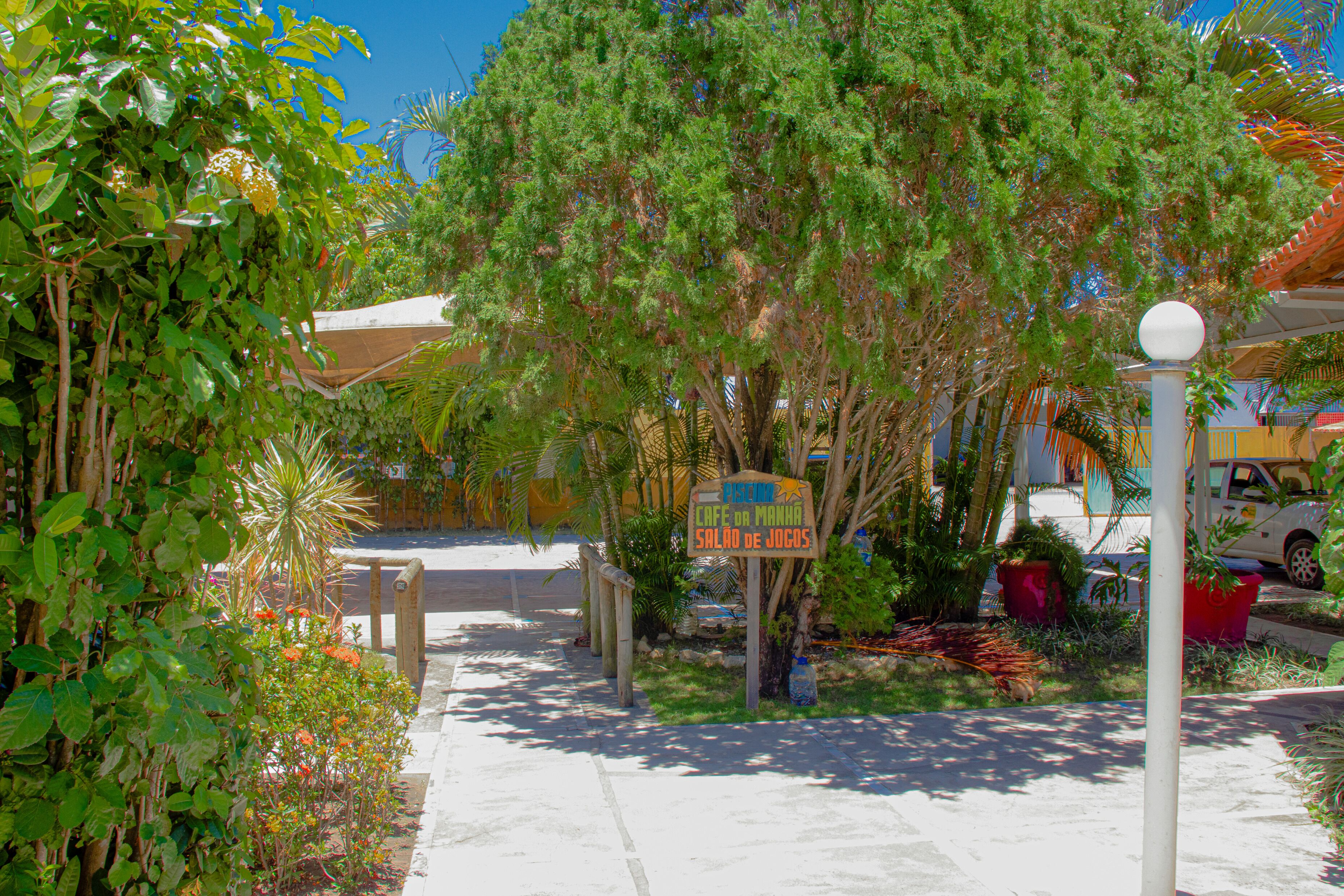 A pathway lined with lush greenery and a sign for Cafe da Mano Salão de Joguos.