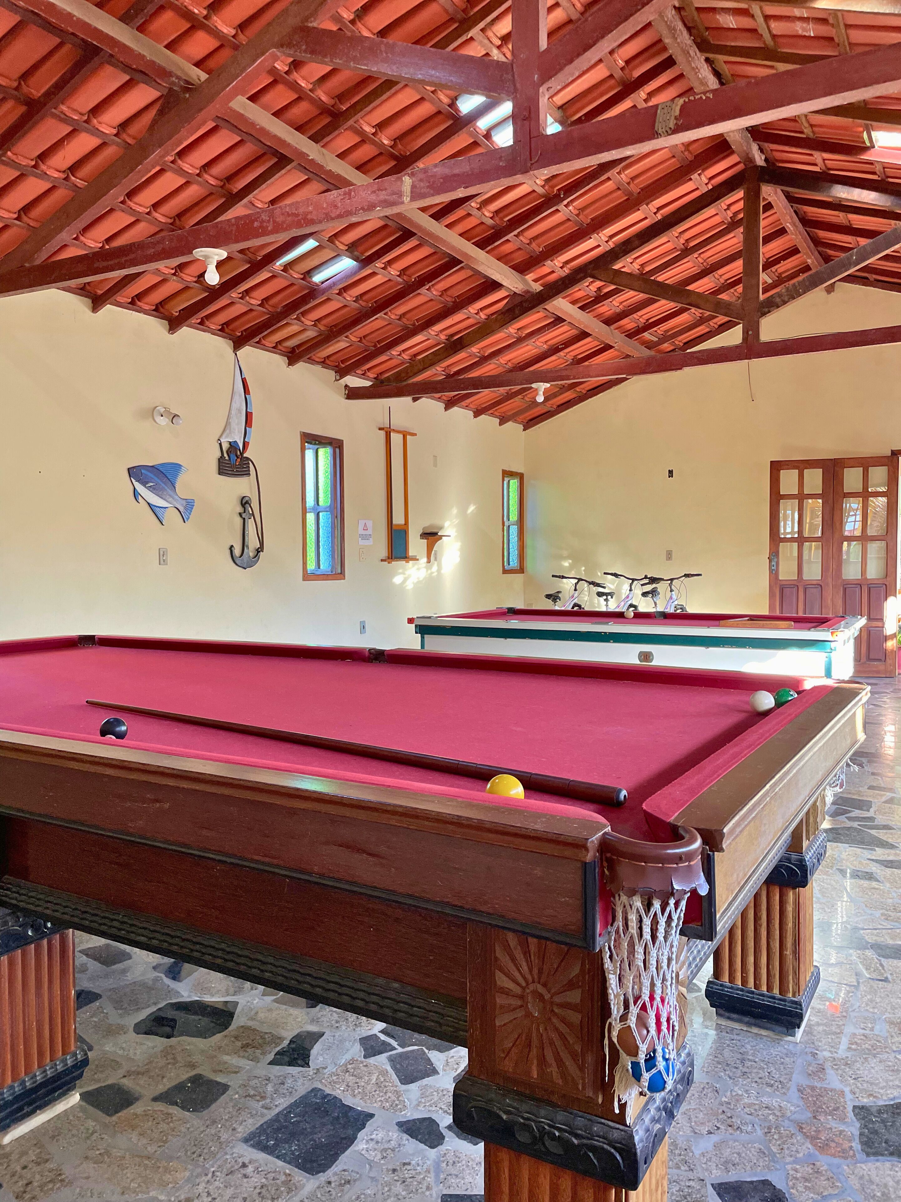 A pool table with a red felt surface, a wooden pool table with a net, and a tiled floor.