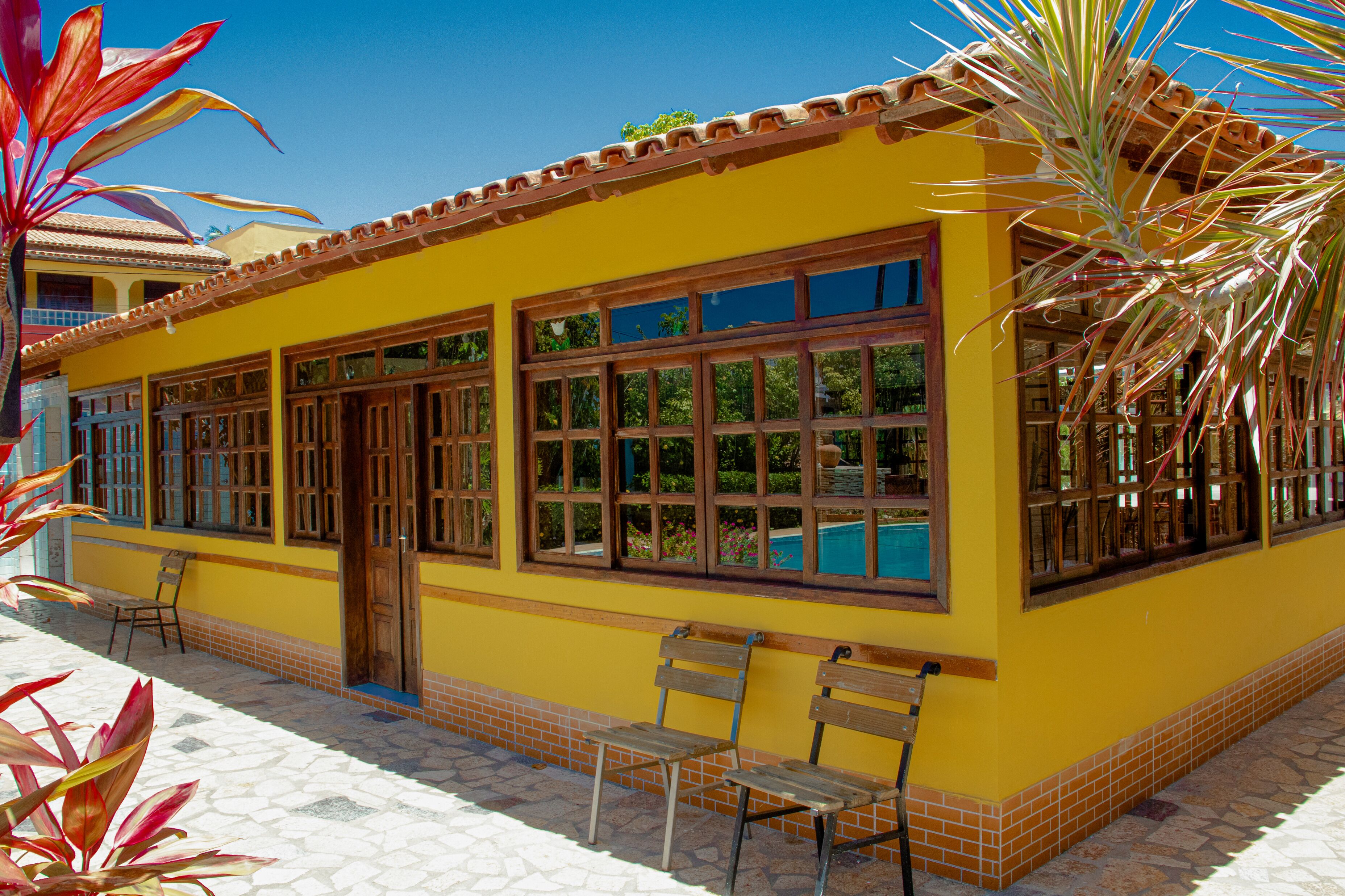 A yellow building with large windows and a door, surrounded by a tiled patio with chairs.