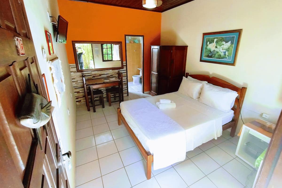 A hotel room with a bed, a desk, a chair, a mirror, a wardrobe, and a ceiling fan.