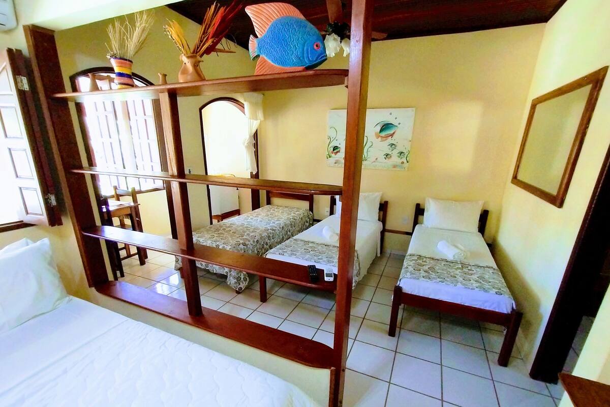 A room with two beds, a wooden bed frame, a small table, and a chair. There is a window with curtains, a wall with a painting, and a door.