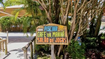 A sign for 'Piscina Cafe da Manha Salão de Jocs' surrounded by tropical plants.