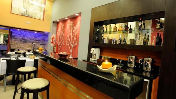 A bar area with a black countertop, bar stools, and a variety of bottles and glasses. - Hotel Osam (Buenos Aires)