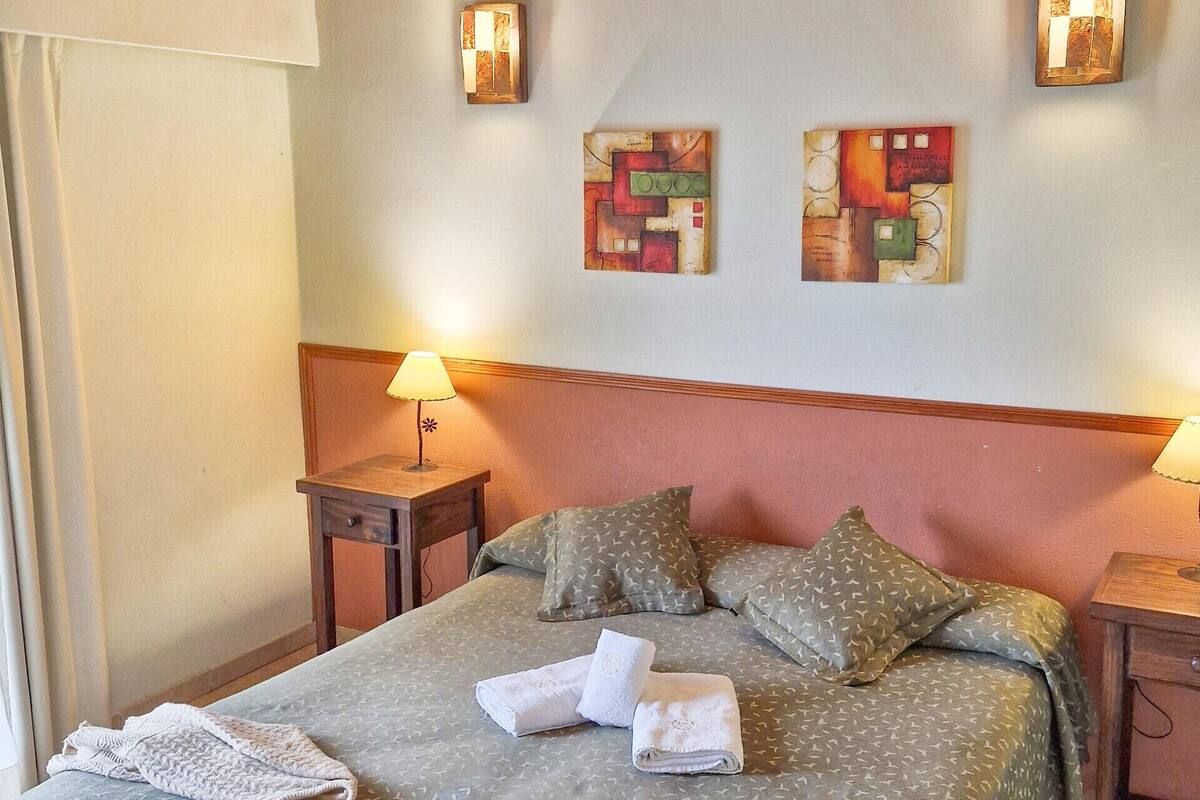 Un lit bien fait, avec des oreillers, une lampe de chevet et un chapeau posé sur le lit.