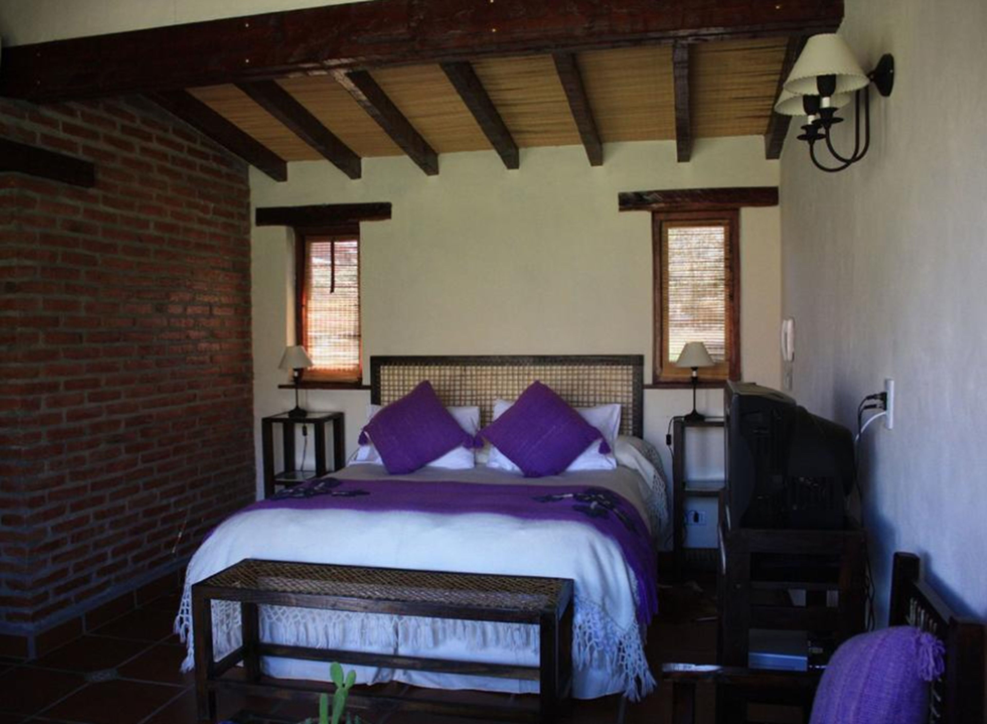 A bedroom with a bed, two bedside tables, a nightstand, a bench, and a wall-mounted lamp.
