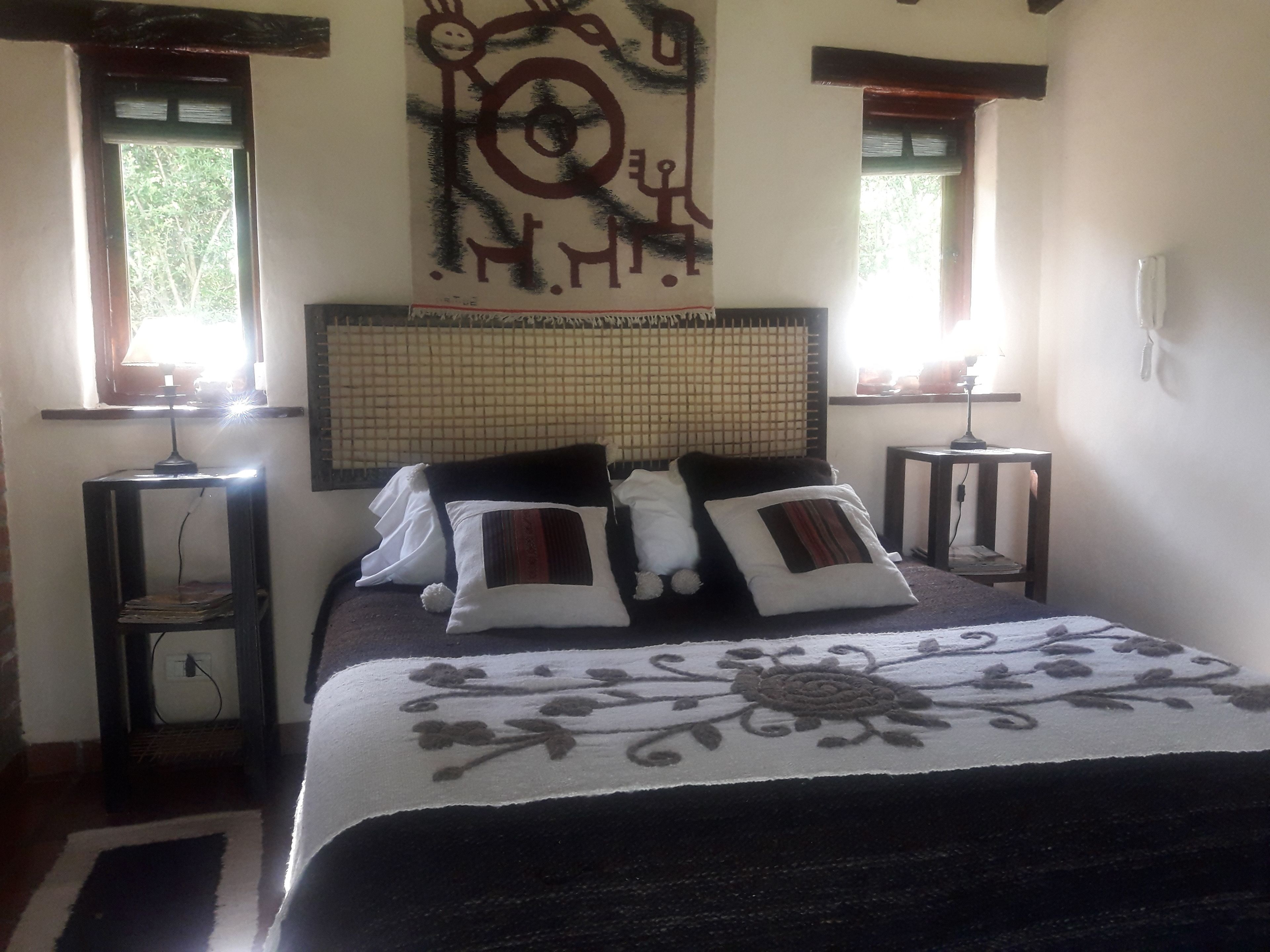 A bedroom with a bed, two bedside tables, a wall-mounted artwork, and a window with blinds.
