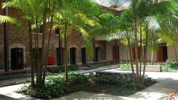 Un patio con palmeras, un edificio de piedra con arcos y un pequeño jardín.