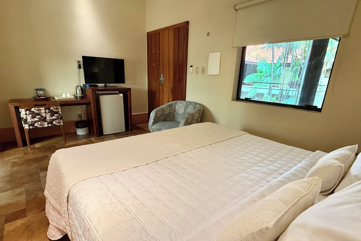 A hotel room with a large bed, a television, a desk with a computer, and a small refrigerator.
