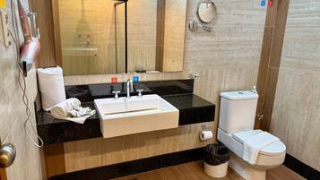 A modern bathroom with a black countertop, white sink, and toilet. There is a towel and a trash can on the floor.