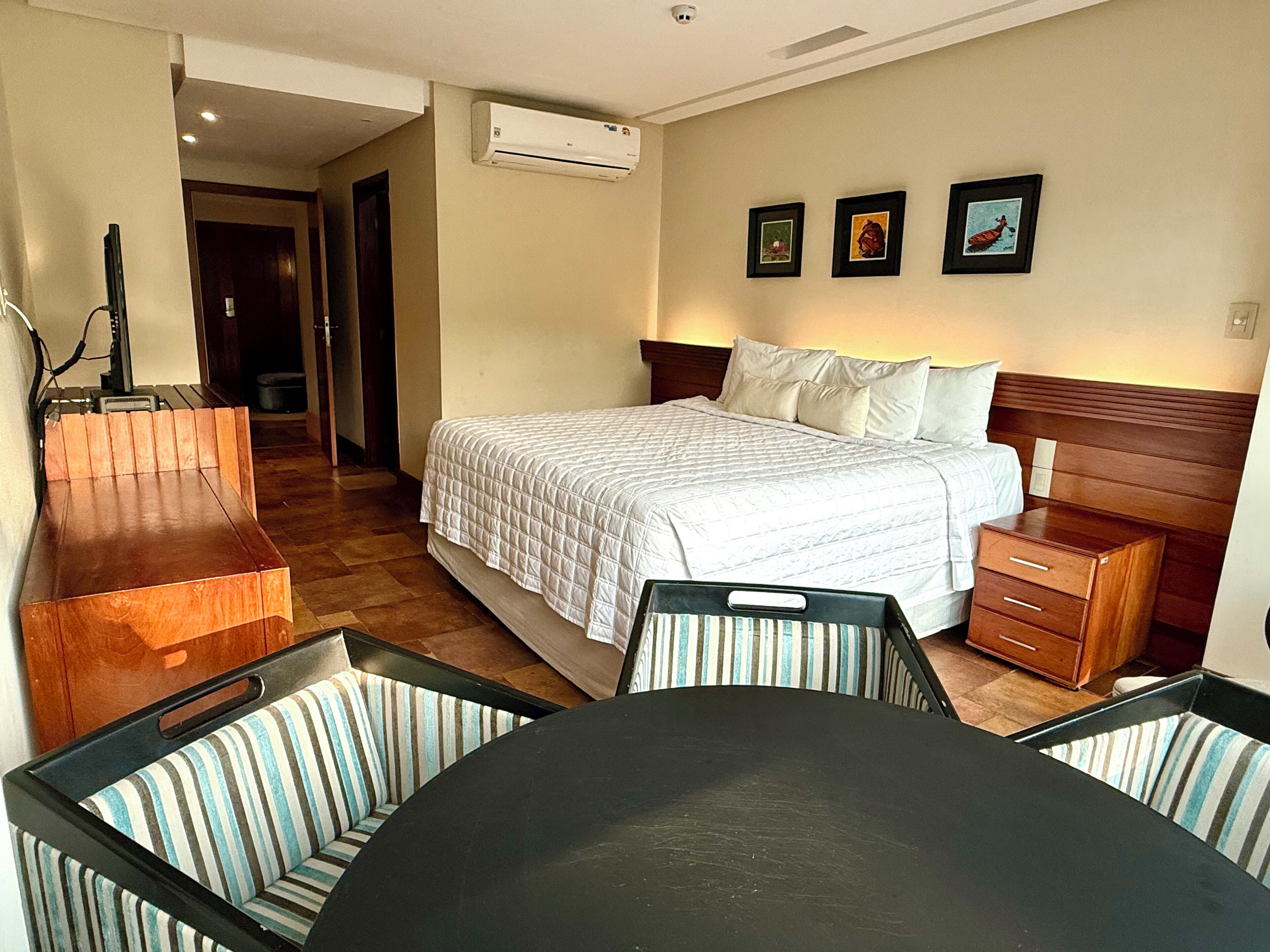 Una habitación de hotel con cama, escritorio, silla, mesa y un armario pequeño.