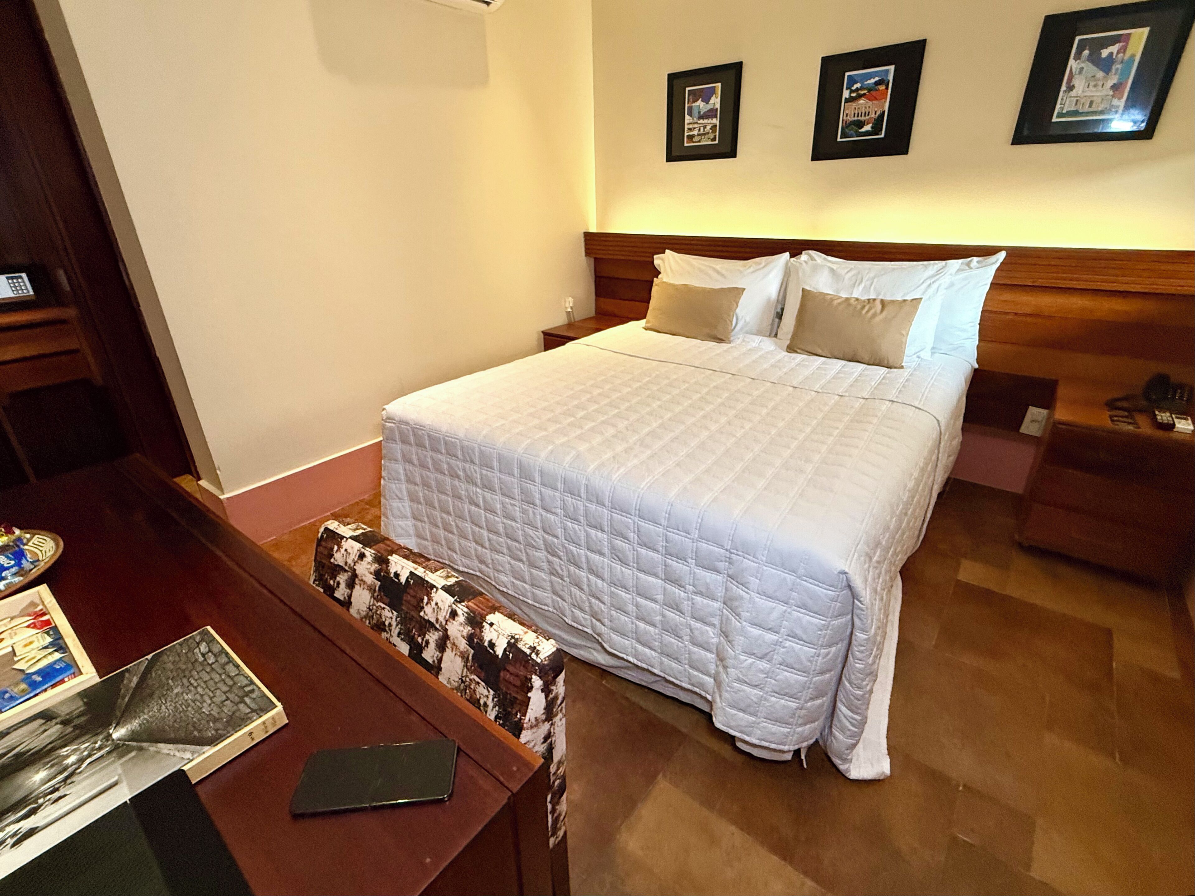 A neatly made bed with a white quilt, a wooden headboard, and a nightstand with a lamp.