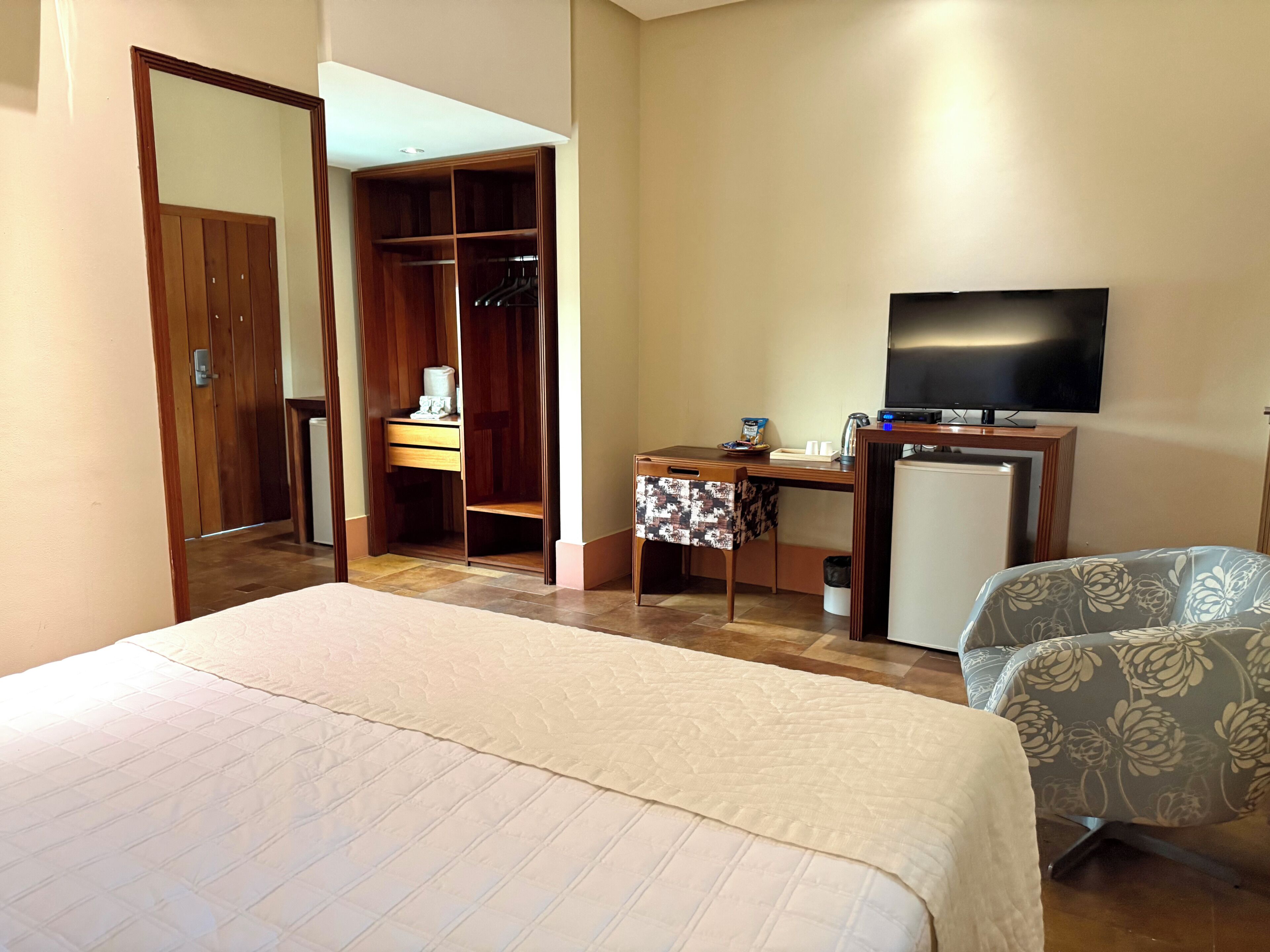 A hotel room with a bed, a desk with a television, a wardrobe, and a chair.