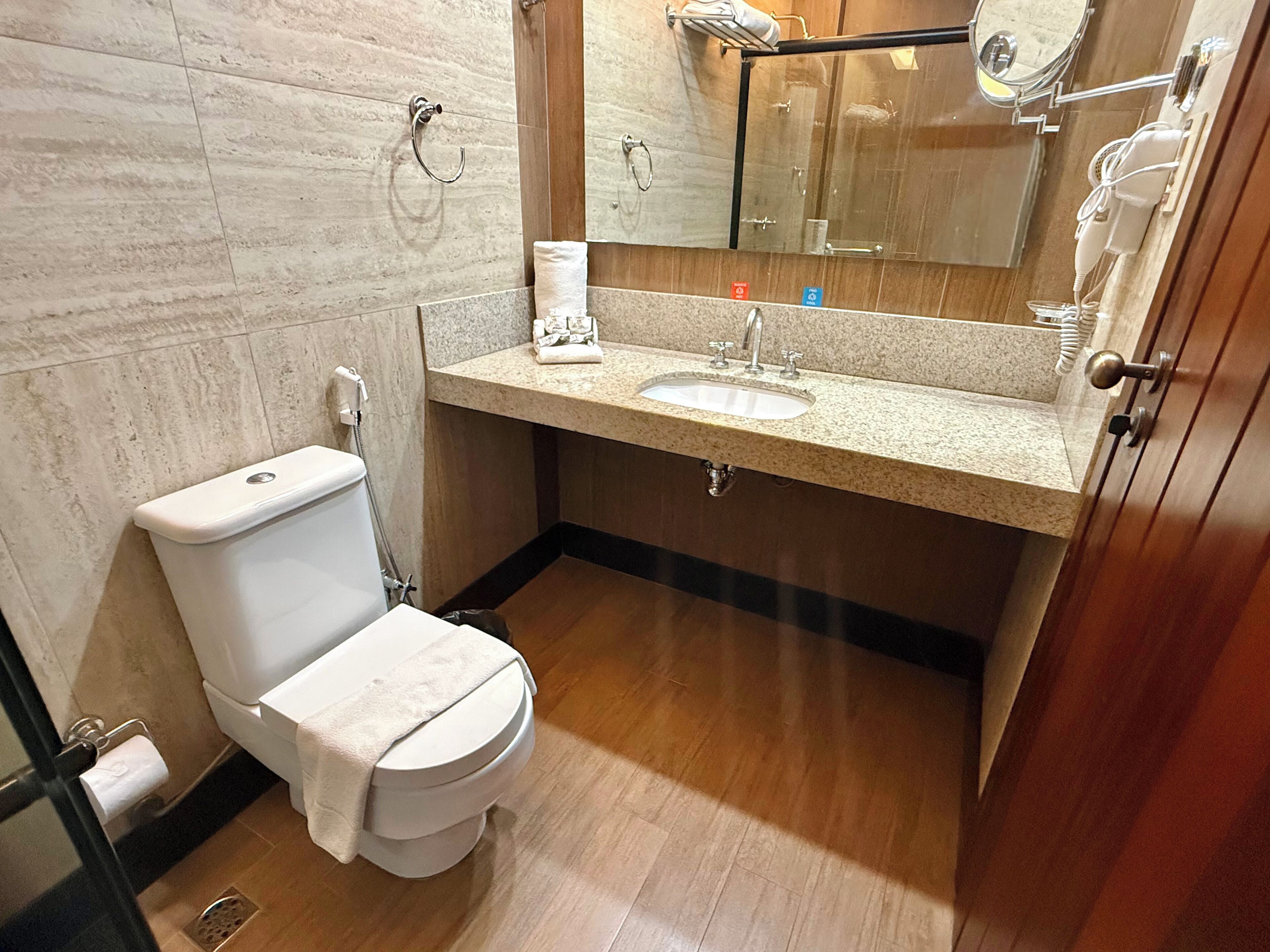 Un baño con inodoro, lavamanos, espejo y toallero.