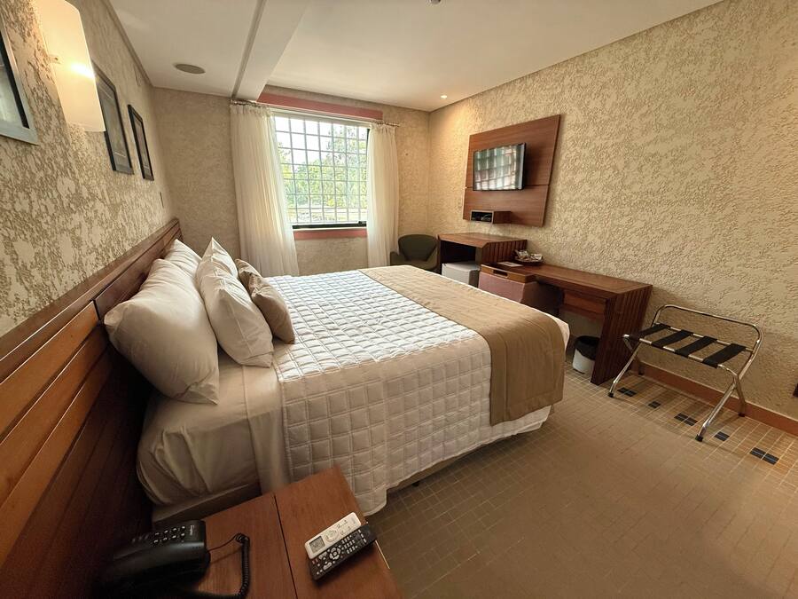 A hotel room with a bed, a desk, a chair, a TV, and a window with curtains.
