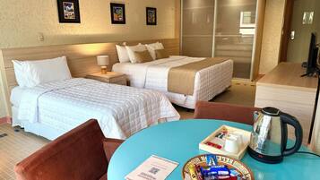 Quarto de hotel com duas camas, uma mesa de centro com petiscos, chaleira e armário com portas deslizantes.
