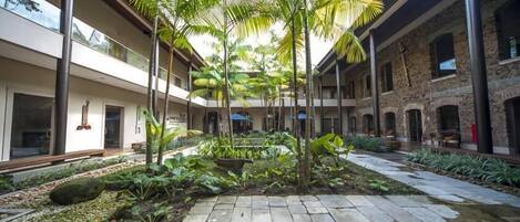 Een binnentuin met een fontein in het midden, omgeven door palmbomen en beplanting, met stenen paden en een combinatie van moderne en traditionele architectuur.