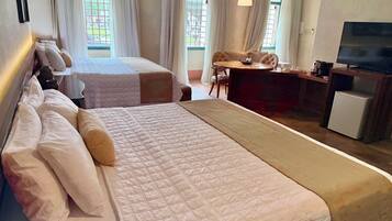Ein Hotelzimmer mit zwei Betten, einem Schreibtisch, einem Fernseher und großen Fenstern mit Vorhängen.