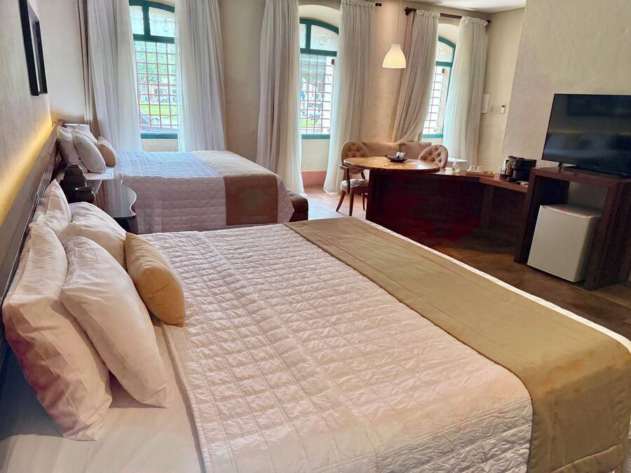 Ein Hotelzimmer mit zwei Betten, einem Schreibtisch, einem Fernseher und großen Fenstern mit Vorhängen.