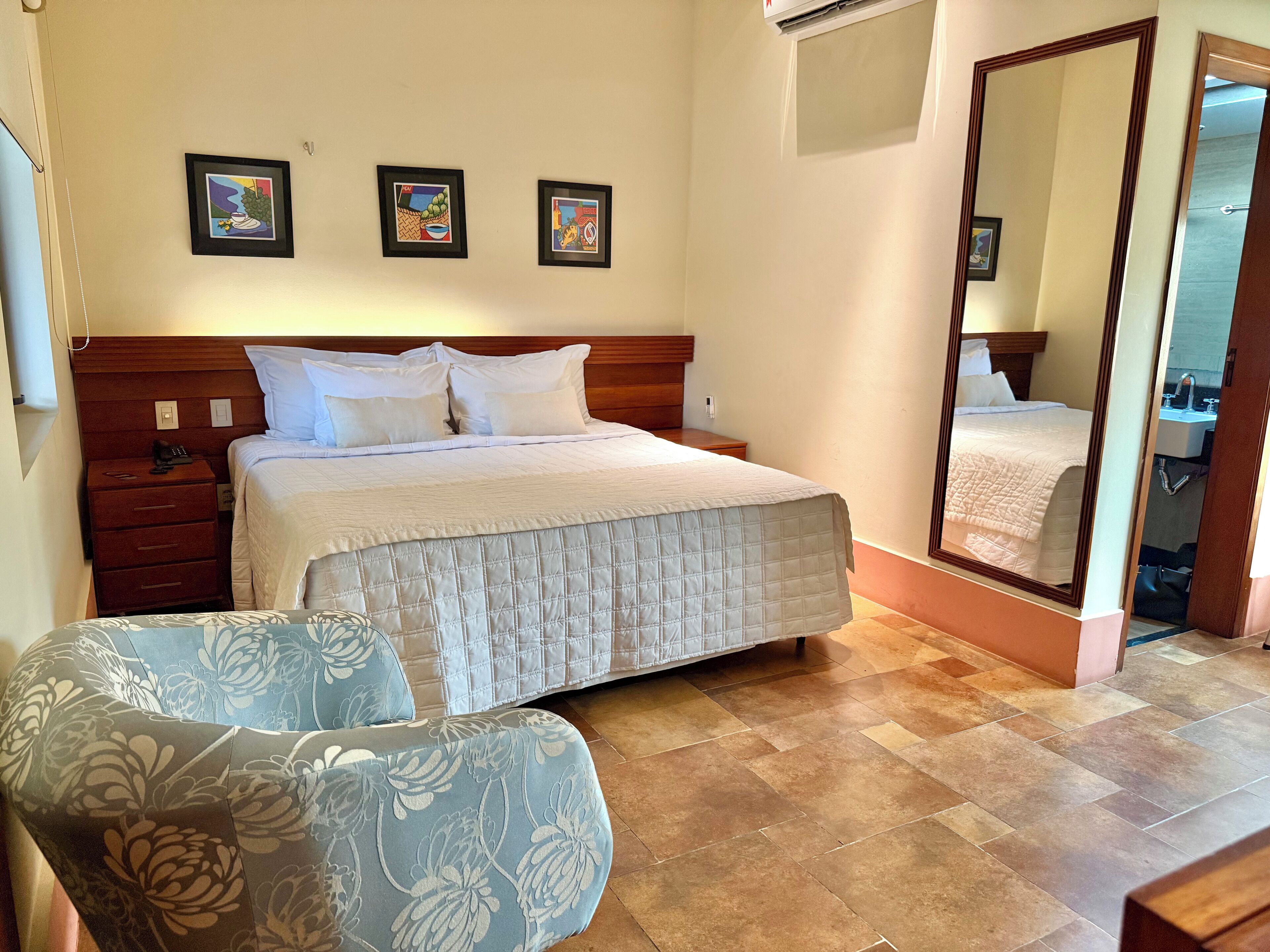 A hotel room with a bed, a nightstand, a chair, and a large mirror.