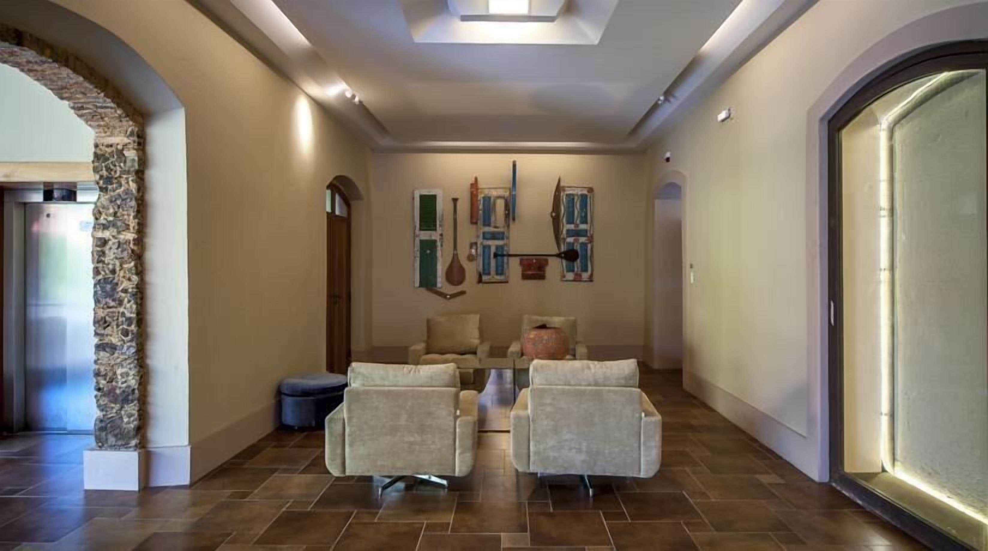 A spacious hallway with a stone accent wall, two armchairs, a large vase, and a door with a glass panel.