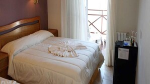 Ett hotellrum med en stor säng, ett träfärgat sänggavel, ett nattduksbord, en lampa, en minibar och utsikt över balkongen.