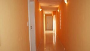En lång, smal hall med orange väggar och ett glänsande golv, som leder fram till en dörr i slutet.