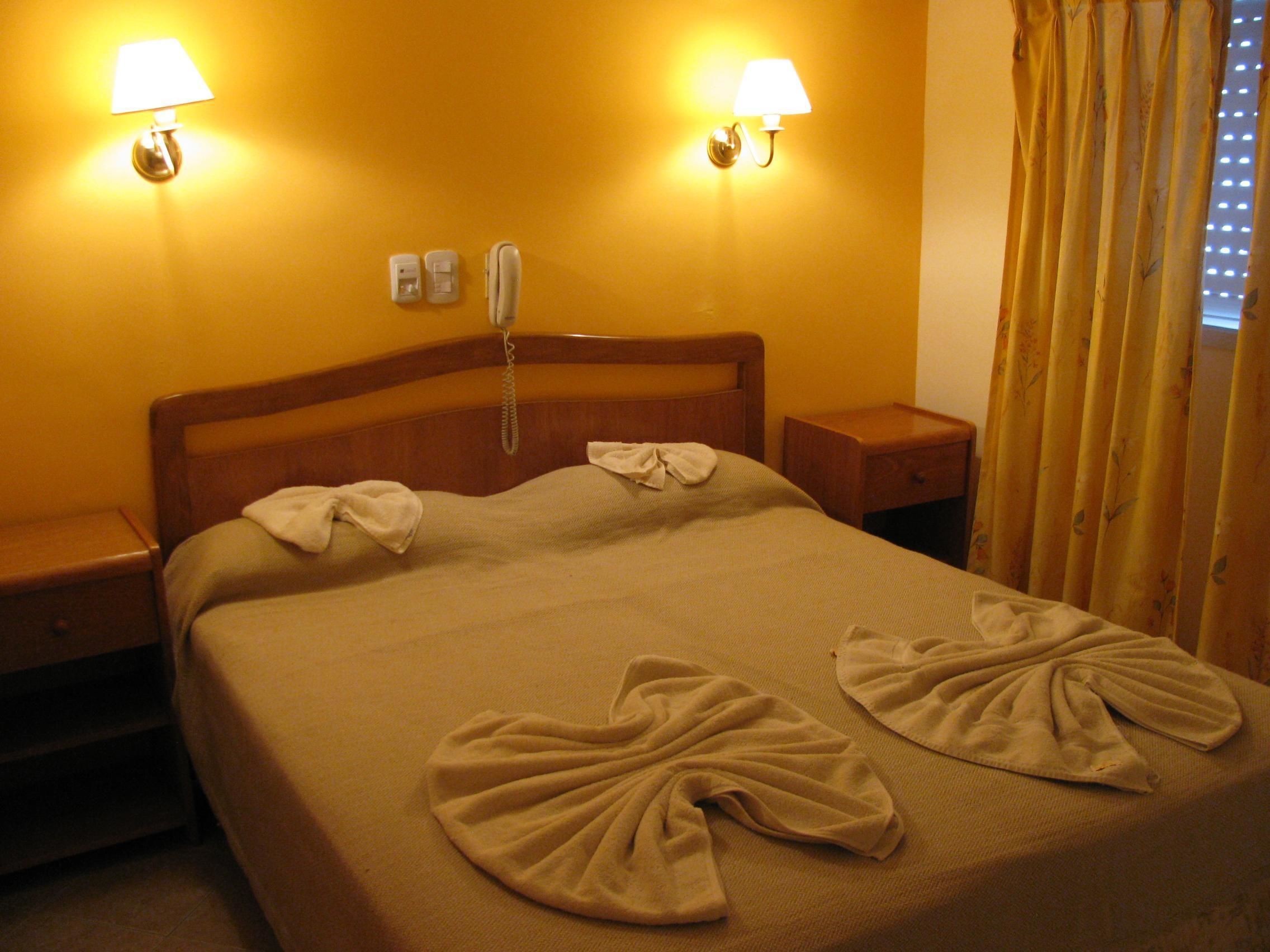 A hotel room with a bed, two bedside lamps, a telephone, and a window with curtains.