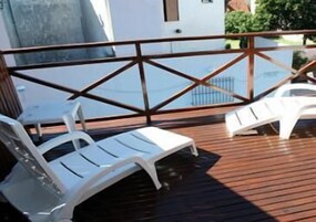 Terraza de madera con sillones blancos y barandilla de cristal.