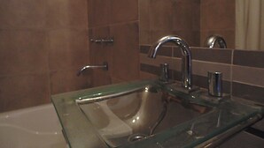 A bathroom with a glass sink, a mirror, and a shower area. - Catamarca Suites Land (Rosario)