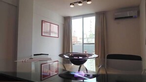 A modern hotel room with a glass dining table, a black chair, a small black table, a picture frame, and a window with curtains. - Catamarca Suites Land (Rosario)