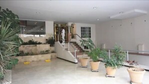 Un espacio interior amplio con una escalera que lleva a un nivel superior, rodeado de plantas en macetas y un gran ventanal.