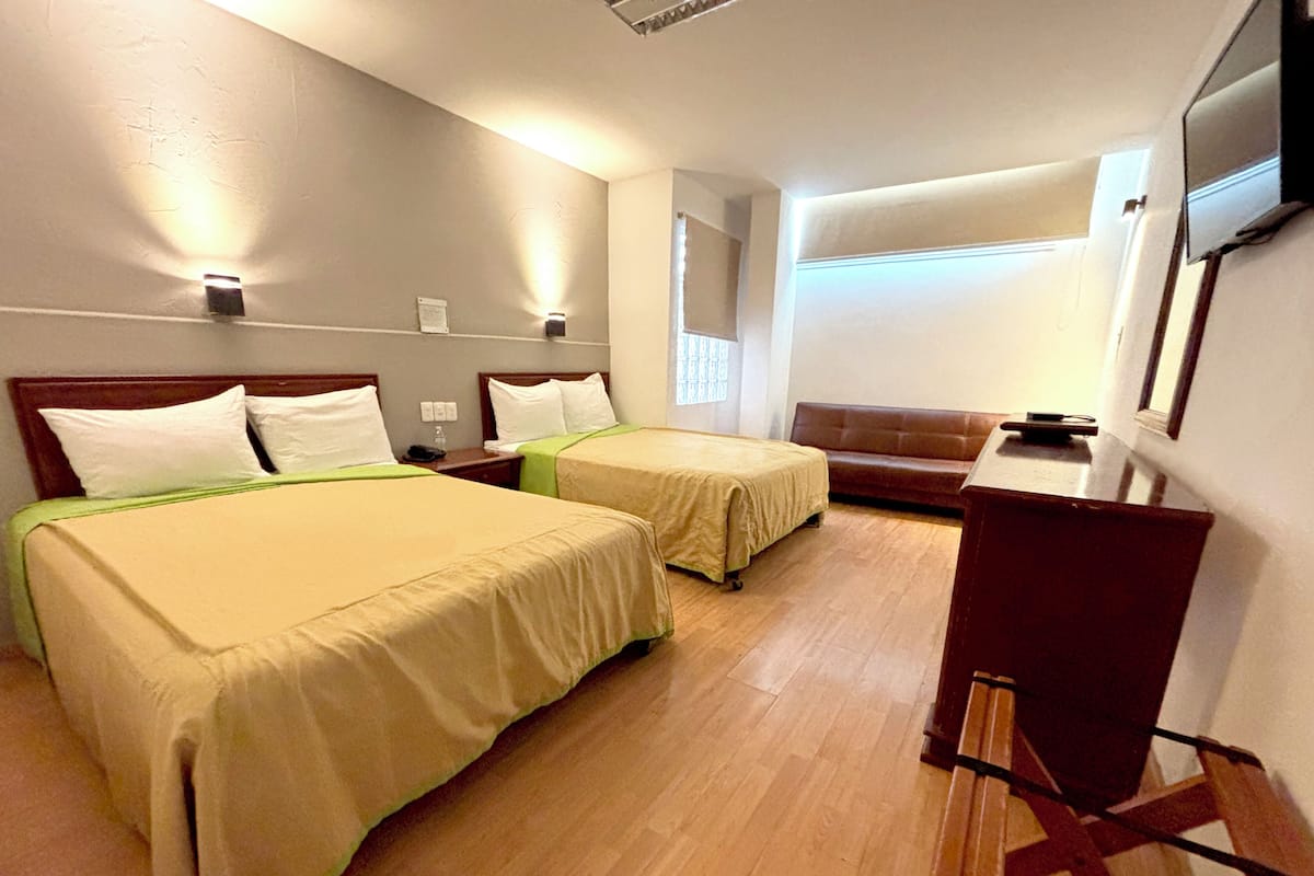A hotel room with two beds, a desk, a chair, a TV, and a window.