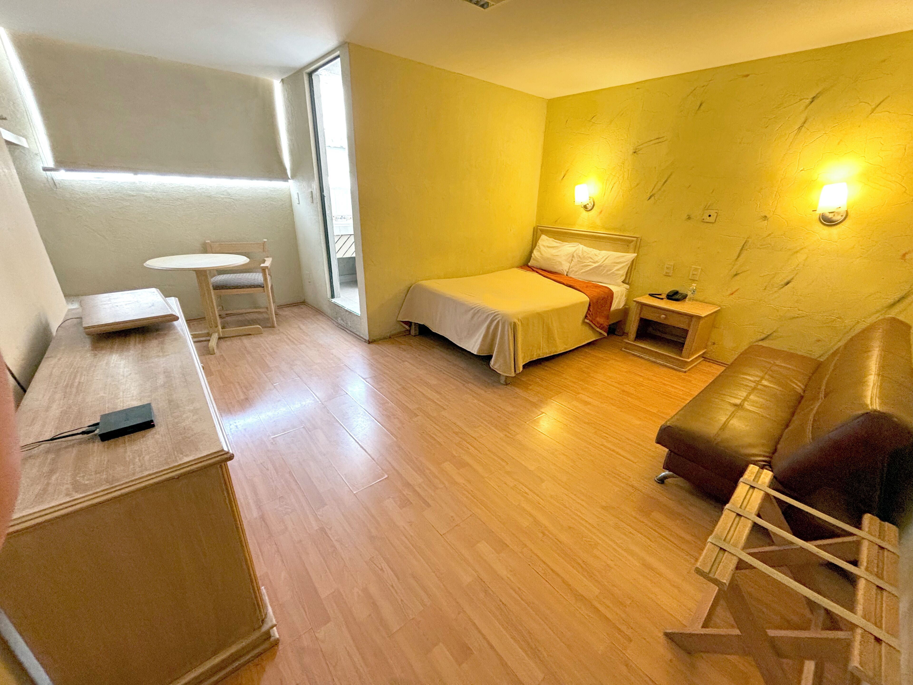 A small, well-lit room with a bed, a desk, a chair, and a sofa.
