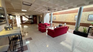 Un vestíbulo espacioso con techo alto, mostrador de recepción, asientos rojos y una planta grande.
